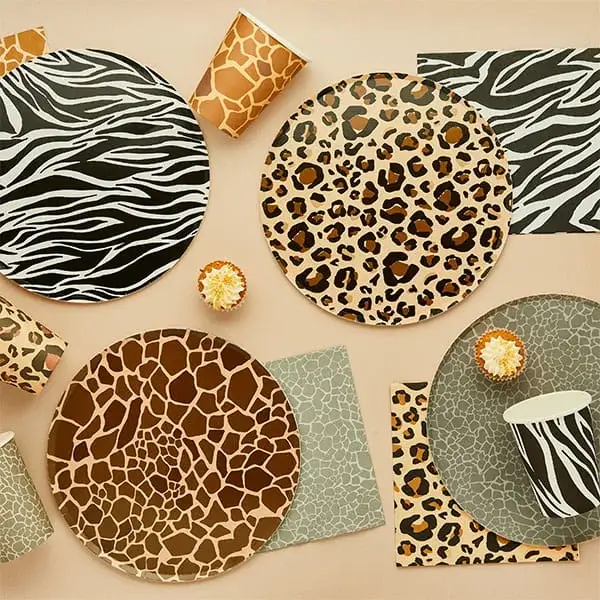 Animal print party tableware featuring zebra, leopard, and giraffe patterned plates, cups, and napkins on a neutral background